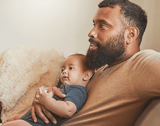 A man holds his baby at his chest - both people are looking off to the left, as if they are watching TV outside of the frame