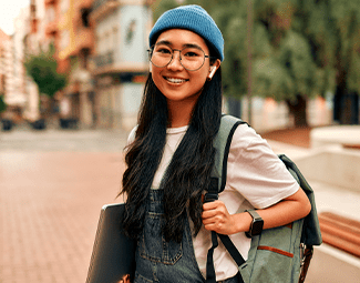 A young woman carrying a backpack and a laptop is smiling at the camera