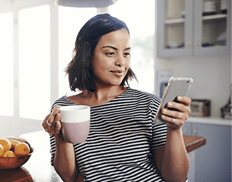 A woman holding her cell phone and a cup of coffee - she appears to be reading her phone